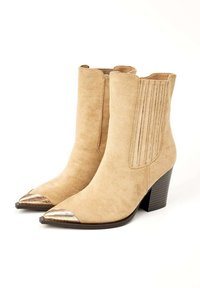 Bottines en suède beige à bout pointu, avec un accent métallique à la pointe et des panneaux latéraux texturés. Talon empilé pour une hauteur supplémentaire.