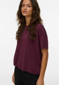 Burgundy stickad t-shirt med korta ärmar, rund halsringning och lös passform, tillsammans med svarta byxor. Mjuk textur och slät finish.