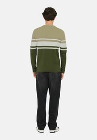 Gebreide trui met horizontale strepen in kaki, wit en groen, gecombineerd met zwarte jeans en witte sneakers.
