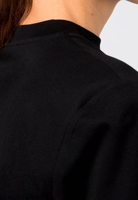 Musta puuvillainen T-paita, jossa on pyöreä pääntie ja lyhyet hihat. Kangas näyttää pehmeältä, sileältä ja siinä on vähäisiä saumauskohteita.