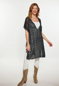 Tunică neagră croșetată, cu decolteu în V, mâneci scurte și modele verticale. Asortată cu pantaloni albi și cizme cowboy maro deschis.