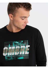 Sudadera negra con cuello acanalado, adornada con una gran impresión gráfica en tonos de turquesa y plata que dice "OMBRE."