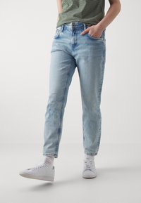 Vaqueros de mezclilla azul claro con un corte relajado y puños en los tobillos. Diseño clásico de 5 bolsillos y textura desgastada. Combinados con zapatillas blancas.