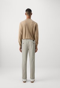 Herreoutfit bestående af en beige, langærmet trøje og lysegrå bukser. Bukserne har baglommer og er parret med hvide sko.