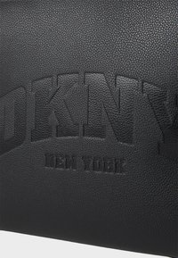Zwarte, gestructureerde leren oppervlak met grote, gebogen "DKNY" en kleinere "New York" tekst eronder.