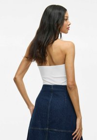 Top bianco senza spalline abbinato a una gonna in denim scuro a vita alta. La gonna presenta cuciture visibili e un design a campana.