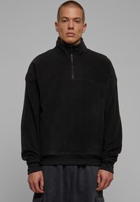 Svart fleece genser med høy krage og halv-glidelås. Har ribbestrikkede mansjetter og en avslappet passform. Minimalistisk design og myk tekstur.