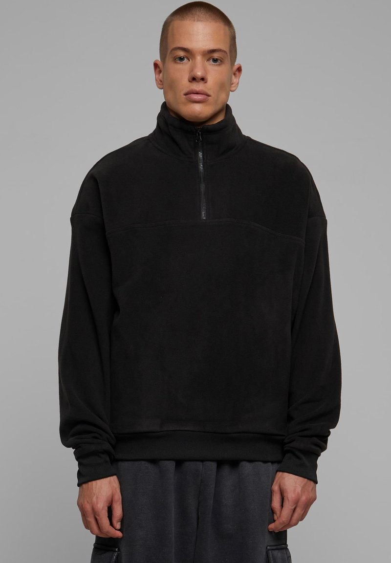 Svart fleece genser med høy krage og halv-glidelås. Har ribbestrikkede mansjetter og en avslappet passform. Minimalistisk design og myk tekstur.