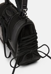 Svart sneakers med en kombination av läder och nät. Anmärkningsvärda detaljer inkluderar snörning och en texturerad sula med "SM"-logotyp.