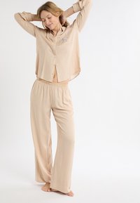 Beżowy, w paski komplet piżamy z koszulą na guziki z kieszenią oraz dopasowanymi spodniami z elastycznym pasem, wykonanymi z miękkiej tkaniny.