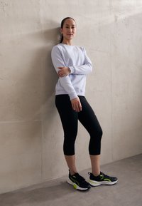 Hellblaues Sweatshirt, schwarze Capri-Leggings und schwarze Sneakers mit grünen Akzenten. Das Outfit hat eine lockere Passform und ein einfaches Design.
