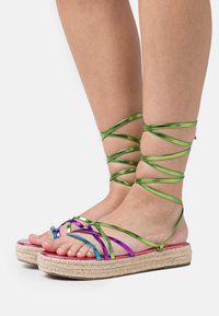 Sandales multicolores à brides avec des lanières métalliques vertes et violettes ; semelle intérieure réfléchissante rose ; semelle plateforme en jute tissé.