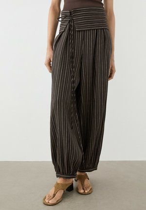 Pantaloni neri a gamba larga con righe verticali bianche, cintura a fascia in vita alta, polsini alla caviglia, indossati con sandali con tacco aperti marroni.