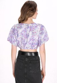 Blüten-Top mit Puffärmeln in Flieder- und Pastellfarben; mit einem gerafften Saum. Kombiniert mit einem hoch taillierten schwarzen Jeansrock.