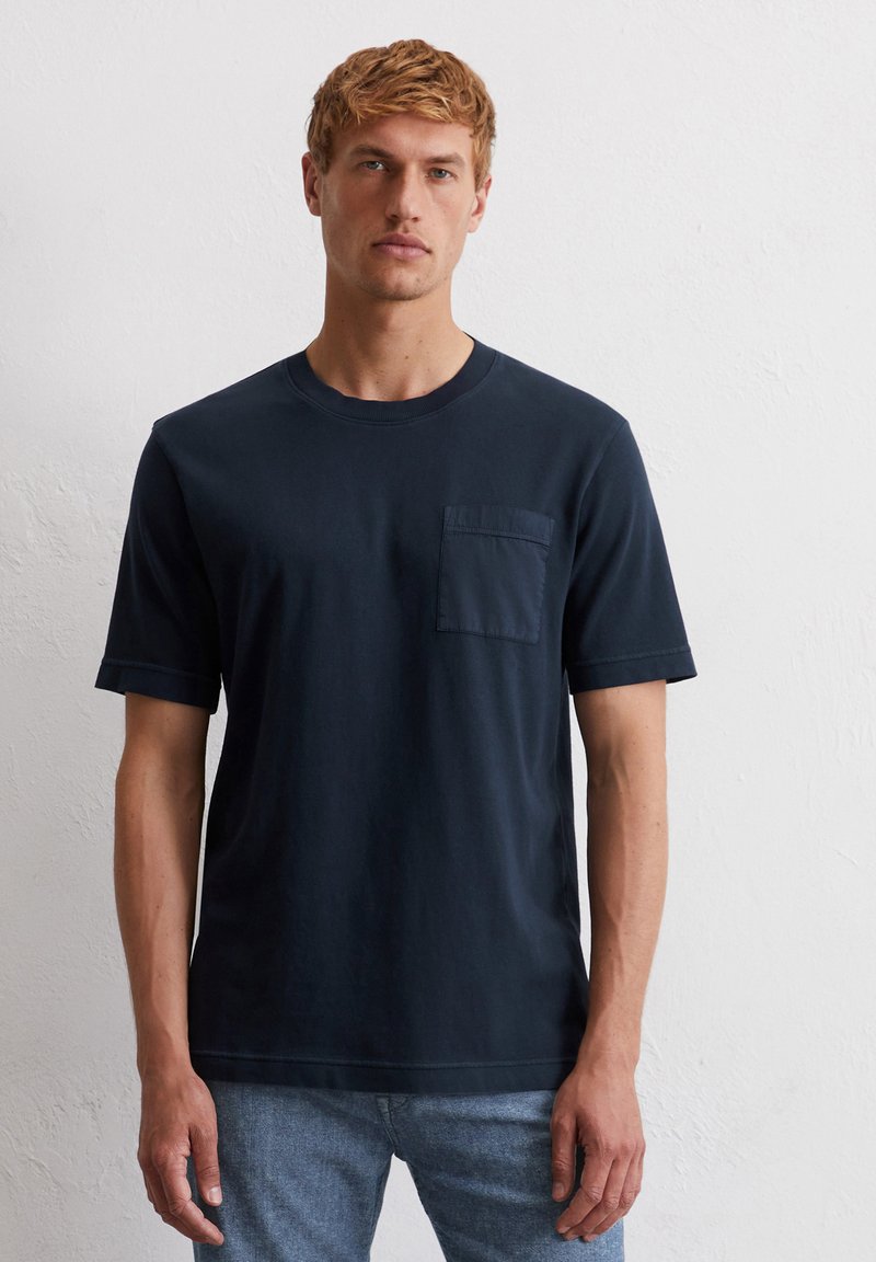 Marineblauwe katoenen t-shirt met ronde hals, korte mouwen en een borstzak. De stof is glad en heeft een lichte stretch.
