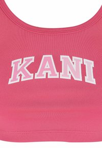 Sujetador deportivo rosa con textura acanalada. Presenta un llamativo logotipo "KANI" en blanco y rosa claro. Cuello redondeado y banda elástica en la parte inferior.