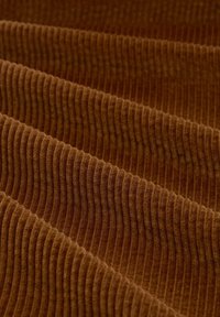 Bruin geribbeld stof met een pluizige textuur, dat parallelle richels heeft die horizontaal lopen en een golflijk patroon over het materiaal creëren.