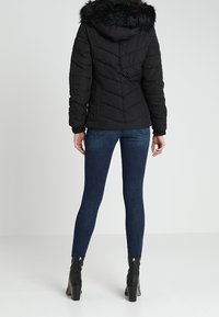 Svart fuskpälsjacka med huva, chevronstickning, ihopparat med mörkblå skinny jeans och svarta stövlar med klack.