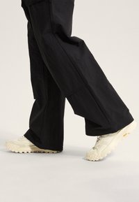 Witte chunky sneakers met textuurzolen, gecombineerd met losse zwarte broek met zijzakken en een gladde stofafwerking.