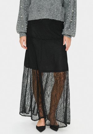 Black lace maxi skirt with sheer overlay. Features scalloped hem and layered design. Worn with a gray sweater and pointed-toe flats.