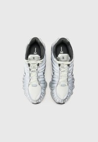 White and silver sneakers with a textured mesh upper, distinctive sole design, and contrasting black accents. Includes lace-up closure.