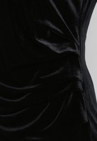 Robe en velours noir présentant une texture lisse et douce avec un design à drapés superposés. Vue en gros plan mettant en valeur la couleur riche et les plis élégants.