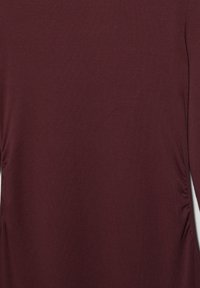 Chemise à manches longues rouge foncé avec une texture lisse et un léger froncé sur les côtés près de la taille.
