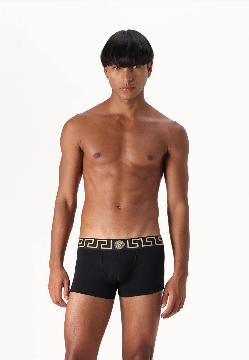Black boxer briefs with a gold Greek key pattern on the waistband and a round logo detail, made from soft, stretchable fabric.