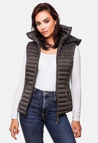 Donkergrijze gewatteerde vest met capuchon, met gestikte textuur, ritssluiting aan de voorkant en zakken, gedragen over een wit shirt en blauwe jeans.