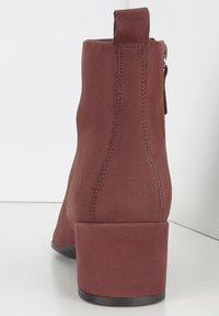 Botín de ante rojo oscuro con tacón cuadrado, cremallera trasera y detalles de costura a lo largo de las costuras. Textura suave, diseño minimalista.