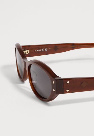 Lunettes de soleil rondes en écaille avec verres foncés et clous dorés en forme de losange sur les branches.