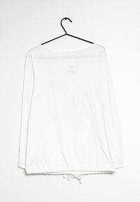 Witte top met lange mouwen, lichtgewicht stof, ronde hals, gegatherde zoom met koord, hangend aan een zwarte haak tegen een effen achtergrond.