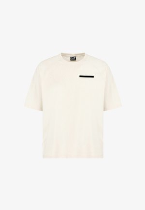 T-shirt a maniche corte di colore beige chiaro con scollatura a girocollo e un accento rettangolare nero sul petto. Tessuto liscio con una vestibilità rilassata.