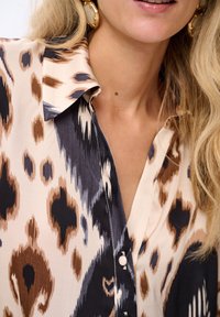 Button-up blouse in lightweight fabric with a beige, brown, and navy leopard print pattern. Features a classic collar and subtle sheen.