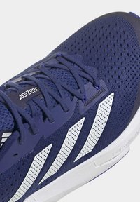Chaussure de sport bleu marine avec des bandes blanches perforées, des lacets bleu marine et une tige en mesh respirant avec une étiquette "ADIZERO" sur la languette.