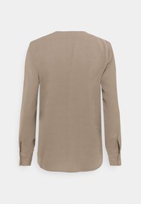 Blouse beige à manches longues avec poignets boutonnés vue de dos sur un fond blanc uni.