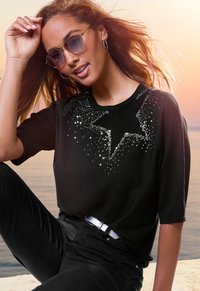 Black t-shirt with short sleeves featuring a sparkling star design made of sequins across the chest, paired with black pants and a metallic belt.
