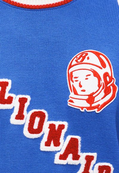 Μπλε πουλόβερ με κεντημένο κείμενο σε κόκκινο και άσπρο. Διαθέτει σήμα με θέμα το διάστημα με φιγούρα που φορά κράνος. Το κείμενο γράφει «Billionaire Boys Club».