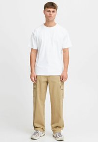 Witte katoenen T-shirt met korte mouwen, gecombineerd met tan cargobroek met zijzakken. Het schoeisel heeft een meerkleurig patroon.
