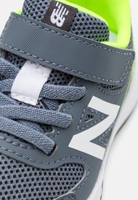 Baskets de sport grises avec un design en mesh, accents blancs et doublure intérieure vert fluo. Équipées d'une sangle velcro et de lacets texturés pour un ajustement sécurisé.