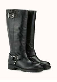 Bottes noires en cuir montantes avec une texture lisse, dotées d'une sangle avec une boucle en argent et des clous décoratifs, ainsi qu'une semelle en caoutchouc robuste.