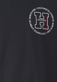 Námořnická modrá bavlněná tričko s kulatým logem s písmenem "H" v bílé, červené a modré barvě, a textem s názvem "Columbus Avenue" a "Od roku 1985."