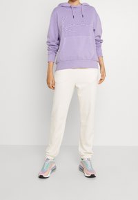 Lila huvtröja med ficka fram och broderad design, ihop med krämfärgade joggers och flerfärgade sneakers.