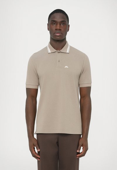 Polo beige en tissu tricoté avec un col classique, présentant des rayures et un petit logo sur la poitrine. Manches courtes, ourlet droit.