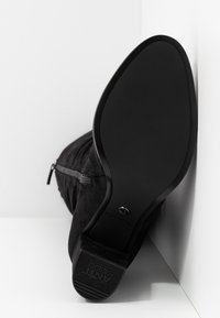 Black suede ankle boot with a rounded toe and a textured rubber outsole, featuring a side zipper closure for ease of wear.