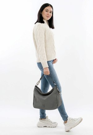 Borsa hobo grigia con un tessuto testurizzato, forma tondeggiante e tracolla corta. Il modello indossa un maglione a treccia crema e jeans di un blu chiaro.