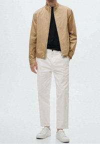 Tanjakke med ståkrave, sort skjorte, hvide bukser og hvide sneakers; glat tekstur og minimalistisk design uden mønstre.