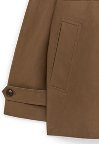 Mouw van een bruine jas met een riemdetail met knoop en een verticale rechthoekige paspelzak op het lichaam van de jas.