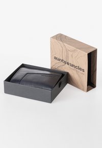 Portafoglio in pelle blu navy all'interno di una scatola nera, con superficie texturizzata e design minimalista, confezionato in una scatola di carta kraft con un motivo a linee.