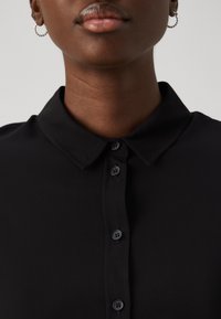 Black button-up shirt with a classic collar, featuring a smooth texture and four matching buttons down the front.